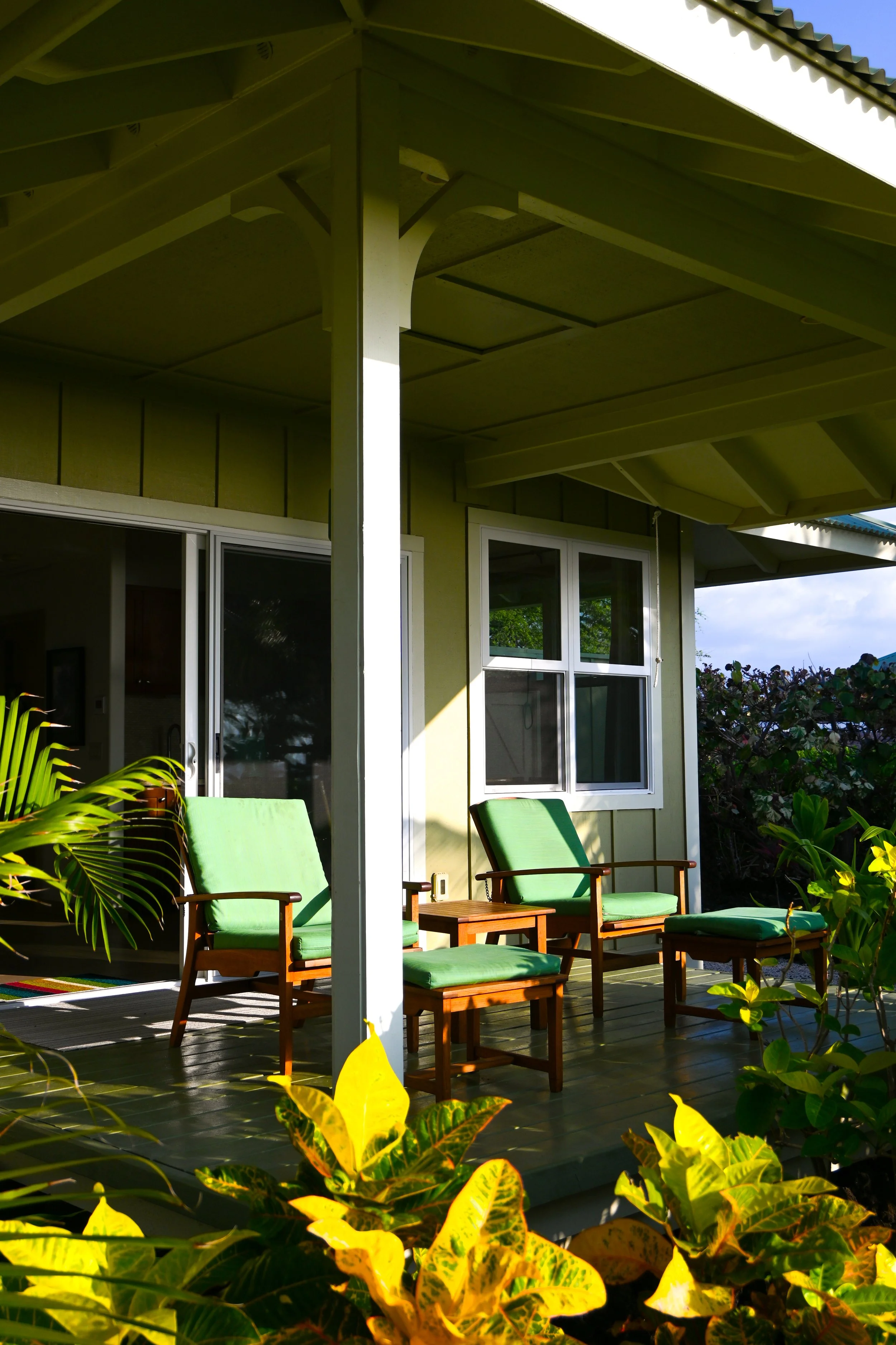Covered lanai with teak chairs and ottoman surrounded by tropical plants